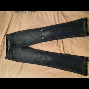 Mörkblå jeans med slitningar - Säljer ett par mörkblå jeans i bra skick med coola slitningar på knäna. De har en tight passform och är perfekta för en avslappnad stil. Jeansen är lågmidjade och har en klassisk femficksdesign. Perfekta för både vardag och fest! De är rätt så långa då jag är 180