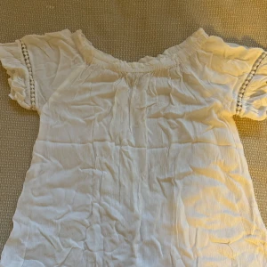 Vit blus med spetsdetaljer - Säljer en söt vit blus i storlek 152 för 12-åringar. Blusen har korta ärmar med fina spetsdetaljer och en smockad halsringning. Perfekt för sommarens varma dagar eller som en söt detalj till en festlig outfit.