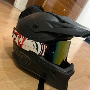 Raven hjälm - Använd under två moppesäsonger, funkar bra för både moppe, motorcykel, cross och cykling! Fint skick och visir följer med. Lite sminkfläckar på insidan, men tyget går att ta ut och tvätta vid önskemål. Nypris för både hjälm och visir tillsammans skulle jag tro går på runt 3200kr