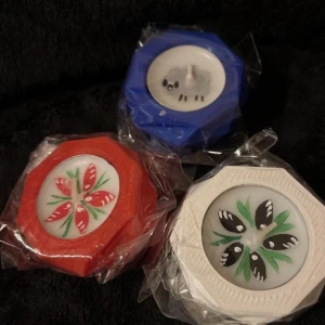 Färgglada ljusstakar med blommönster - Säljer tre ljusstakar i olika färger: röd, blå och vit/lila.  Varje värmeljus har ett unikt blommönster på ljuset. Perfekt för att liva upp köket med lite färg och stil. Ljusstakar med värmeljus är i nytt skick och fortfarande i plastförpackning. Motivet flyter med på värmeljusen