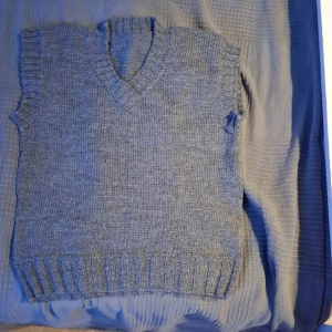 Grå stickad väst - Säljer en mysig grå stickad väst med v-ringning. Perfekt för lager-på-lager under höst och vinter. Den har ribbade kanter vid ärmhål och nederkant för en snygg passform. Passar både till vardags och lite finare tillfällen. Ett måste i garderoben för den stilmedvetna!