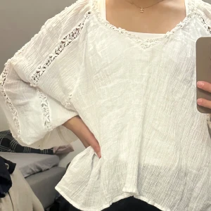 Vit blus med spetsdetaljer - Säljer en superfin vit blus med v-ringning och spetsdetaljer längs ärmarna och ryggen. Blusen har en luftig passform perfekt för vår och sommar. Den är gjord i ett lätt och bekvämt material som känns skönt mot huden.