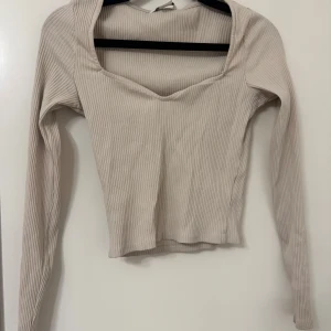 Beige ribbad topp - Säljer en superfin beige ribbad topp med lång ärm och v-ringad design. Den är i mycket bra skick och inte använd fåtal gånger, säljer då den blivit för liten för mig❤️