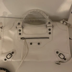 Vit handväska med dragkedja - Säljer en snygg vit handväska i skinn med coola detaljer. Väskan har en praktisk dragkedja framtill och robusta handtag. Perfekt för både vardag och fest! 👜✨