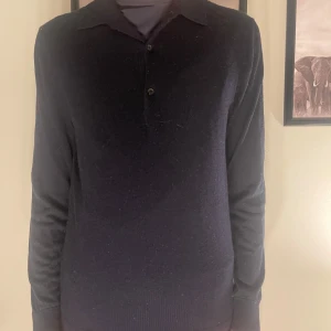 Svart långärmad pikétröja - Säljer en stilren svart långärmad pikétröja i mycket bra skick. Perfekt för både vardag och festliga tillfällen. Tröjan har en klassisk krage och knappar framtill. Passar bra till både jeans och chinos.