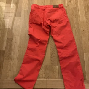 Röda byxor från GANT - Säljer ett par snygga röda byxor från GANT i modellen Tyler. De har en något lägre midja och en regular fit med raka ben. Perfekta för en avslappnad men stilren look. Passar bra till både vardag och fest!