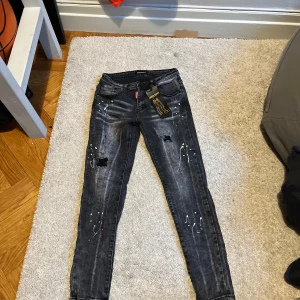 Svarta jeans med slitningar - Säljer ett par svarta jeans med coola slitningar och vita färgstänk. De har en tight passform och är perfekta för en avslappnad stil. Jeansen har en klassisk femficksdesign och är i bra skick. Perfekta för både vardag och fest!