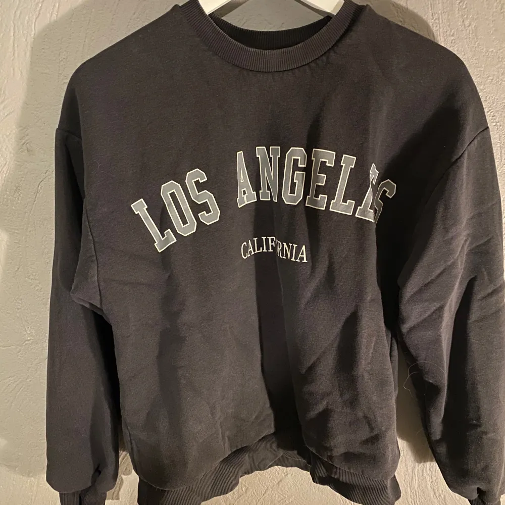 Säljer en snygg mörkgrå sweatshirt med texten 'Los Angeles California' i vitt&grått på framsidan från gina tricot. Tröjan har en normal passform och är perfekt för en avslappnad stil. Den är i mycket bra skick och passar perfekt för höst och vår. Superbekväm och lätt att matcha med jeans eller joggers! (PM OM DU VILL HA FLER BILDER). Tröjor & Koftor.