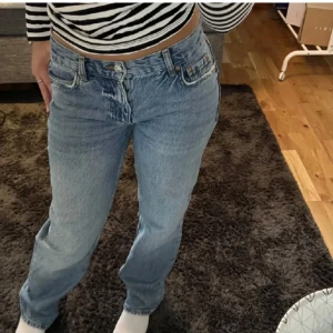 Blå jeans med knappdetalj - Snygga blå jeans med klassisk femficksdesign och knappdetalj framtill. De har en avslappnad passform och är perfekta för en casual look. Passar bra med en randig topp eller hoodie.
