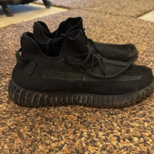 Svarta Adidas Yeezy sneakers - Säljer ett par svarta Adidas Yeezy sneakers med en stilren design. Skorna har en stickad ovandel och en robust sula. Perfekta för en trendig look.