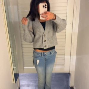 Grå stickad kofta - Säljer en mysig grå stickad kofta med knappar framtill. Koftan är croppad och har långa ärmar, perfekt för en avslappnad stil.