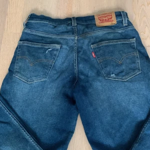 Blå jeans från Levi's - Säljer ett par klassiska blå jeans från Levi's med en loose taper passform. De har en knappgylf och fem fickor. Perfekta för en avslappnad stil.