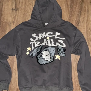 Broken planet space trials hoodie - Cool svart hoodie med texten 'Space Trails' och en dödskalle på framsidan. Har en stor huva och långa ärmar. Perfekt för en avslappnad stil.