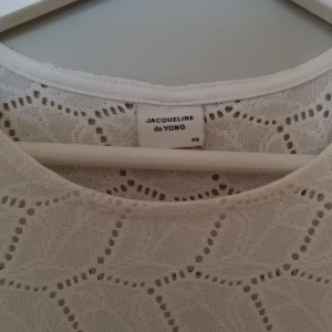 Vit spetsmönstrad topp från Jacqueline de Yong - Säljer en söt vit topp från Jacqueline de Yong i storlek XS. Toppen har ett vackert spetsmönster och korta ärmar, perfekt för en stilren look. Passar bra till både jeans och kjol. 🌸