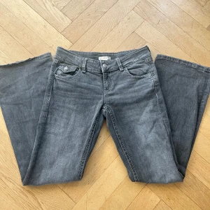 Grå bootcut jeans från Gina Tricot - Snygga grå bootcut jeans från Gina Tricot med dekorativa broderier på bakfickorna. Jeansen påminner av y2k med det detaljerade fickorna. Jeansen har en lågmidjad passform och är tillverkade i ett bekvämt material. Storleken är 158 för barn men passar också om man är petite/ kort storlek 36/34