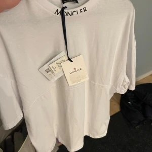 Vit t-shirt från Moncler - Säljer en stilren vit t-shirt från Moncler med logotypen tryckt i svart på baksidan. T-s. Skitsnygg tröja som är oanvänd och är perfekt för en utgång!