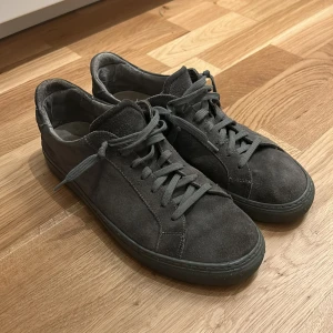 Grå sneakers i mocka - Snygga grå sneakers i mocka med snörning. Perfekta för en stilren look. De har en klassisk design med låg profil och matchande grå sulor. Skorna är ifrån Garment project och ligger ungefär på 1500 nypris. 