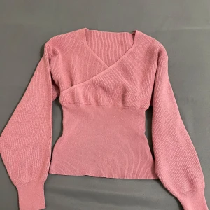 Stickad Tröja  - Säljer en söt rosa omlottopp med långa ärmar. Toppen har en ribbad struktur och en smickrande passform som framhäver midjan. 