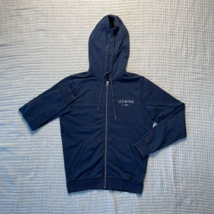 Mörkblå ziphoodie från Lexington - Säljer en stilren mörkblå hoodie från Lexington med dragkedja och justerbar huva. Tröjan har långa ärmar och praktiska fickor framtill. 