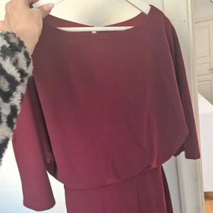 Vinröd klänning - Snygg vinröd klänning med trekvartsärm och en elegant passform. Perfekt för höst och vinter med sin djupa färgton. Klänningen har en enkel design som gör den lätt att styla.