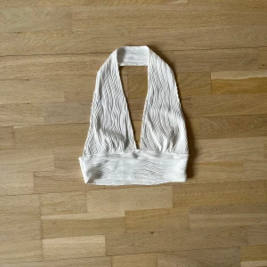 Vit ribbad halterneck topp - Snygg vit halterneck topp med ribbad textur. Perfekt för sommarens varma dagar. Toppen har en stilren design och är lätt att matcha med olika outfits.