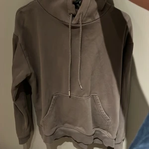 Brun hoodie med ficka - Säljer en brun hoodie med känguruficka och justerbar huva. Perfekt för en avslappnad stil. Den har långa ärmar och en bekväm passform.