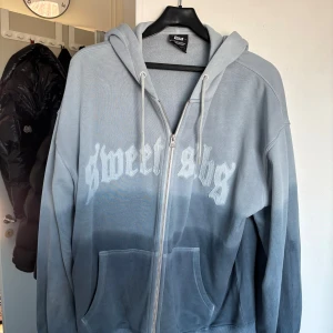 Grå hoodie från Sweet SKTBS - Säljer en snygg grå hoodie från Sweet SKTBS med dragkedja och tryck framtill. Hoodien har en ombre-effekt som går från ljusgrå till mörkgrå och är perfekt för en avslappnad stil. Den har en klassisk passform med långa ärmar och en bekväm huva. Priset kan diskuteras.