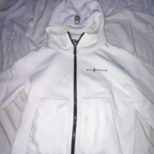Vit zip hoodie från sail racing - Säljer en stilren vit jacka från Sail Racing med dragkedja och huva. Jackan har två praktiska fickor framtill och en diskret logga på bröstet. Perfekt för en sportig look! (Det är storlek 150 men det passar också XXS)