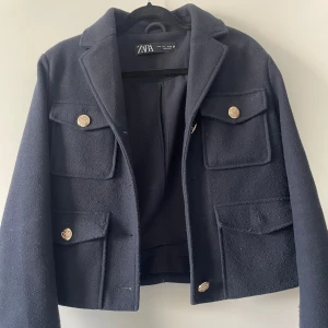 Mörkblå kappa från Zara  - Snygg mörkblå kappa från Zara med guldknappar och flera fickor. Perfekt för en stilren look. Kappan har tyvärr tappat en knapp därav priset, samt att den är lite nopprig! 
