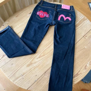 Evisu y2k low waist bootcut jeans med hjärtan och patches - Sååå fina straight leg/bootcut lågmidjade jeans med Evisu-patcjes på bakfickorna i rosa/lila/rött!! Såå unika! Fickorna baktill är igensydda då broderierna e sydda rakt igenom fickorna. Midja 40cm, midja till gren 22cm, innerben 78cm  Vintage, 70tal,90tal, y2k, 2000s, boho chic, rock chic, Ibiza summer, glitter, strass, nitar, studs, rhinestones, bling, paljetter, western, cowboy, fringe, tassle, fransar, läder, genuine leather, suede, mocka, stockholmstyle, Stockholmsstil, wedge boots, marant, 