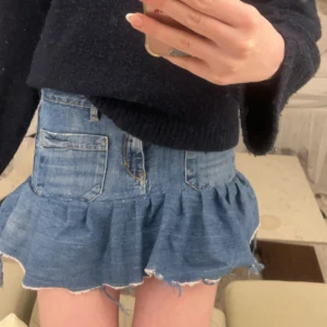 Jeanskjol med volang - Trendig jeanskjol med volangdetalj och rå kant. Kjolen har två stora framfickor och en knappstängning. Perfekt för en avslappnad stil. Skulle säga att den passar ungefär som en XS💕💕