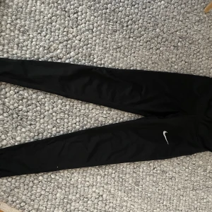 Svarta träningstights från Nike - Snygga svarta träningstights från Nike med en liten logga på benet. Perfekta för träning eller en avslappnad dag. De är tillverkade i ett stretchigt material som ger en bekväm passform.