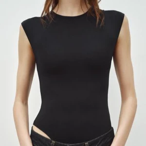 Svart ärmlös bodysuit från Zara - Snygg svart ärmlös bodysuit från Zara i ett glansigt material. 🥰jättebra skick i storlek S! Använd kanske 2 gånger. Perfekt för att skapa en stilren look. Den har en enkel design med rund halsringning och knäppning i grenen. 