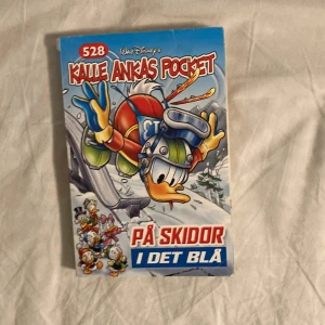 Kalle Ankas Pocket: På Skidor I Det Blå - Kalle Ankas Pocket nummer 528 med titeln 'På Skidor I Det Blå'. Omslaget visar Kalle Anka i skidutrustning på en snöig backe. Perfekt för fans av Kalle Anka och vintersport.