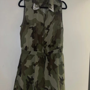Camouflage byxdress från Bik Bok - Snygg ärmlös byxdress i camouflage från Bik Bok. Den har en cool krage dekorerad med glittriga detaljer. Perfekt för en trendig look! Storlek L, passar mer som M