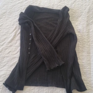 Svart ribbad kofta från Gina Tricot - Säljer en svart ribbad kofta från Gina Tricot i storlek XS. Koftan har långa ärmar och knappar framtill, perfekt för lager-på-lager-stil. Den ribbade strukturen ger en snygg och stilren look. Passar utmärkt till både vardag och mer uppklädda tillfällen. Möts bara upp. Aldrig använd