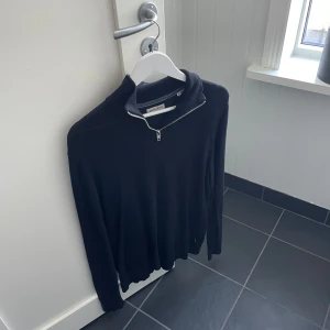 Svart tröja med dragkedja från Jack & Jones - Snygg svart tröja från Jack & Jones med dragkedja vid halsen. Perfekt för en stilren look. Tröjan har långa ärmar och en bekväm passform. Tunn och väldigt skön tröja som passar vad du än ska göra. Inga hål eller skador på den. 