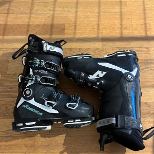 Nordica Speedmachine 3 105 W GW 22/23 - Säljer ett par svarta Nordica Speedmachine 3 105 W GW 22/23 pjäxor med vita och turkosa detaljer. De har flera spännen för optimal passform och är designade för att ge bra stöd och komfort under skidåkning. Nypris 5500kr. Har köpt ett par tur pjäxor och använder därför inte dessa längre. 