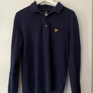 Mörkblå pikétröja från Lyle & Scott - Säljer en stilren mörkblå pikétröja från Lyle & Scott med klassisk krage och knappar framtill. Sitter som S