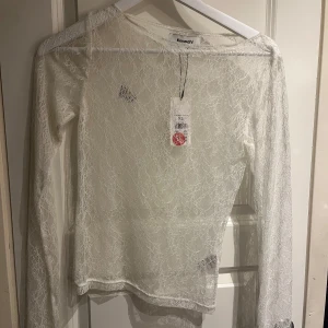 Vit spetsblus från Kappahl - Säljer en elegant vit spetsblus från Kappahl. Blusen har långa ärmar och ett vackert spetsmönster som ger en romantisk känsla. Perfekt för att lägga till en touch av elegans till din garderob. (den svarta fläcken är på dörren) 