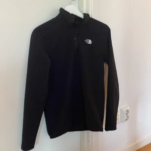 Svart fleece tröja från The North Face - Säljer en svart fleece tröja från The North Face med halv dragkedja och broderad logga på bröstet. Perfekt för kyliga dagar och utomhusaktiviteter. Tröjan har långa ärmar och är supermjuk och bekväm. Den passar även Xs då den är ganska liten. Kan tänka mig att byta mot en i större storlek också.