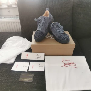 Blå sneakers från Christian Louboutin - Snygga blå sneakers från Christian Louboutin i mocka med ikoniska röda sulor. Skorna har snörning och är dekorerade med nitar på tån för en edgy look. Perfekta för dig som vill sticka ut med stil. Kom med bud! 😁