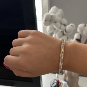 Guldarmband med glittriga detaljer - Elegant guldarmband med glittriga detaljer. Armbandet har en stilren design med små gnistrande stenar längs kanterna, perfekt för att ge en touch av glamour till din outfit.