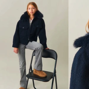 Mörkblå teddyjacka med pälskrage - Snygg mörkblå teddyjacka med en fluffig pälskrage och knappar framtill. Jackan har två stora fickor på bröstet och långa ärmar. Perfekt gör våren. Från Gina Young i stoleken 158