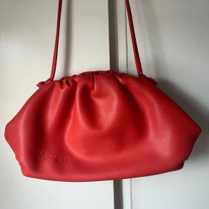 Orange axelväska från K.Cobler - Snygg röd axelväska från K.Cobler i syntetmaterial. Väskan har en stilren design med rynkade detaljer upptill och en smidig axelrem. Perfekt för att ge en färgklick till din outfit.