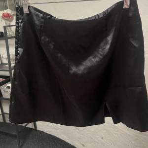 Snygg svart kortkjol i satin. Kjolen har en elegant glansig yta och en klassisk passform som passar perfekt för olika tillfällen. En stilren och tidlös design som är lätt att matcha med olika toppar. Kan inte se storlek men skulle säga att det är en M-L.