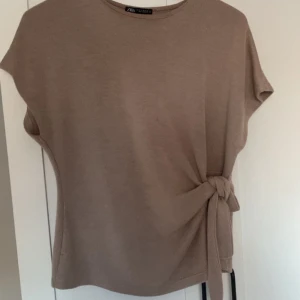 Beige topp från Zara - Säljer beige topp från Zara med korta ärmar och en snygg knytdetalj på sidan. Hör av er om fler bilder eller frågor 💕
