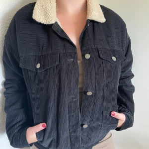 Svart manchesterjacka med teddyfoder från Roxy - Säljer en snygg svart manchesterjacka från Roxy med mysigt teddyfoder. Jackan har en klassisk design med knappar framtill och två bröstfickor. Perfekt för höst och vinter när du vill hålla dig varm och stilren. Jackan är långärmad och har en normal passform.