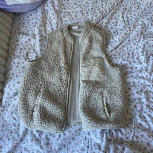 Beige fleeceväst från ONLY - Säljer en supermysig beige fleeceväst från ONLY. Perfekt för kyliga dagar med sin mjuka och varma känsla. Västen har en praktisk ficka på bröstet och två sidofickor. Den är i storlek M och passar perfekt för höst och vinter. Ett måste för garderoben!