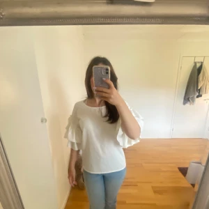 Vit blus från Gina Tricot - Säljer en superfin vit blus från Gina Tricot i storlek 36. Den har korta ärmar med volangdetaljer som ger en romantisk touch. Perfekt för både vardag och fest!